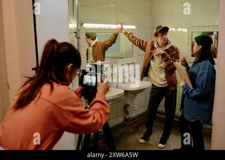 Junger Mann, der zeigt, während er von einem Fotografen in der Badezimmerszene gefilmt wird, während Fotografen Momente in dramatischer Performance mit detailliertem Hintergrund festhalten Stockfoto