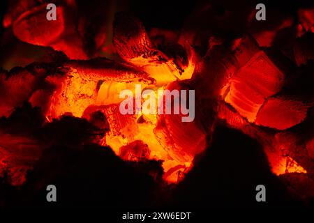 Heiße Kohlen leuchten orange im Dunkeln des Herds. Sie zeigen die Schichtstruktur des Holzes. Nahaufnahme. Stockfoto