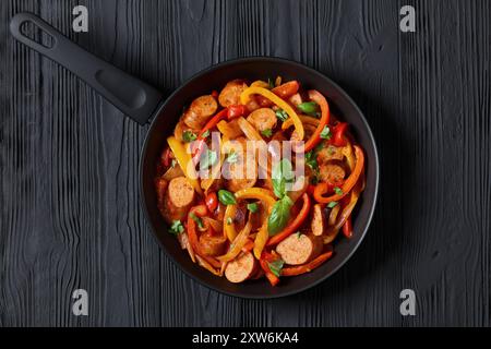 italienische Wurst-Paprika und Zwiebeln in würziger Tomatensoße gekocht, bestreut mit frischem Basilikum und Petersilie auf einer Pfanne auf schwarzem Holztisch, horizontal Stockfoto