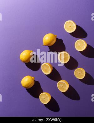 Ganz und halbiert in Zitronen auf violettem Hintergrund mit dramatischen Schatten Stockfoto