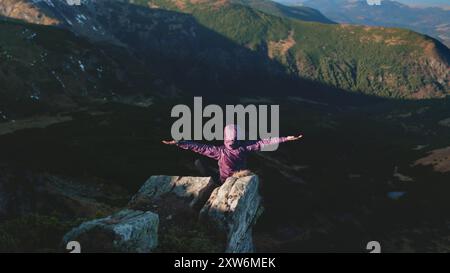 Junger Wanderer sitzt am Rande einer Klippe mit erhobenen Armen und genießt den Blick auf die karpaten in der ukraine Stockfoto