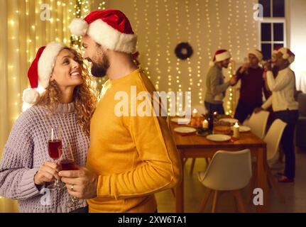 Glückliches, junges Paar, das verliebt ist, trinkt Wein auf einer Weihnachtsfeier mit seinen Freunden Stockfoto
