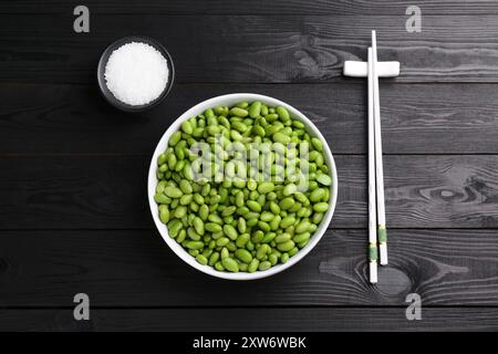 Rohe grüne Edamame-Sojabohnen, Salz und Essstäbchen auf Holztisch, flache Lagen Stockfoto