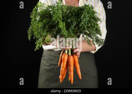 Eine Frau mit reifen Möhren auf schwarzem Hintergrund, Nahaufnahme Stockfoto