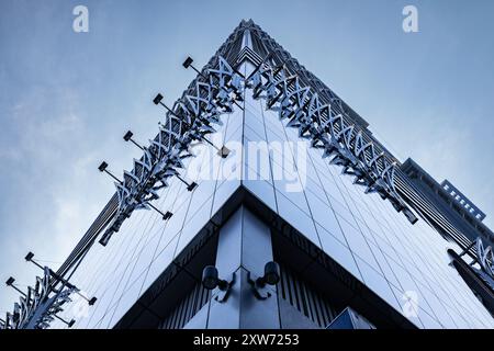 Abgewinkelter Blick auf eine große, mit Fenstern bedeckte Gebäudeecke vor blauem Himmel. Modernes Business Center. Fragment eines Bürogebäudes aus Glas, Futur Stockfoto