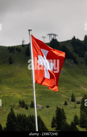 Schweizer Flagge winkt im Wind. Auch die Skilifte eines alpinen Skigebietes sind zu sehen. Sommersaison. Stockfoto