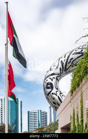 Die Nationalflagge der Vereinigten Arabischen Emirate weht in der Luft vor hohen Gebäuden und dem Museum of the Future Dubai. Skyline-Stadtbild mit modernem Design Stockfoto