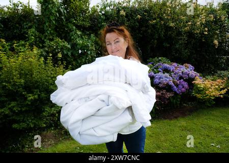 Reife Frau, die einen Haufen trockener, sauberer, weißer Laken hält - John Gollop Stockfoto