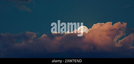 Heller weißer Vollmond, der von hinten aufsteigt, und orangefarbene Wolkenbank als Hintergrund. Stockfoto