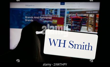 Person mit Smartphone und Logo des britischen Einzelhandelsunternehmens WH Smith plc (WHSmith) vor der Website. Schwerpunkt auf dem Display des Telefons. Stockfoto