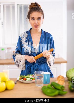 Hausfrau in einem Bademantel mit einer Nadel in den Händen in der Küche Stockfoto