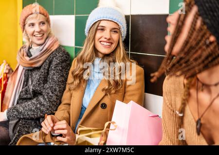 Gruppe von verschiedenen jungen Freundinnen an der U-Bahn-Station nach dem Wintereinkauf. Fröhliche Millennials in farbenfroher, warmer Kleidung, mit Taschen, mit geselligem Beisammensein Stockfoto