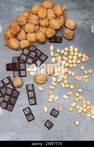 Hausgemachte Schokoladenzutaten auf einem Tisch. Nüsse und Schokolade aus nächster Nähe. Dunkle Schokolade, Pistazien, Nussbaum und Haselnuss vor dunklem Hintergrund Stockfoto