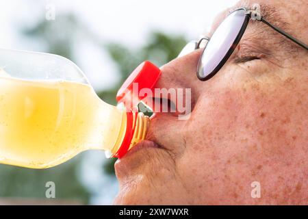 Ärgernis neuer Flaschenverschluss, Mann trinkt aus einer Plastikflasche mit fest verbundenem Deckel, Kappe stört, München, August 2024 Deutschland, München, August 2024, Ärgernis neuer Flaschenverschluss, Mann trinkt aus einer Plastikflasche mit fest verbundenem Deckel, Kappe stört an der Nase, seit Juli gilt die EU-Verordnung, dass Einweg-Plastikflaschen einen fest verbundenem Deckel besitzen, so soll Plastikmüll vermeiden werden, Softdrinks mit neuen Verschlusskappen, Senioren, Rentner, Ü60, Sommer, Bayern, *** nerviger neuer Flaschenverschluss, Mann trinkt aus einer Plastikflasche mit fest befestigtem c Stockfoto