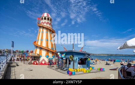 Farbenfroher Helter Skelter und Strandshop am Strand am heißen Sommertag in Weymouth, Dorset, Großbritannien am 16. August 2024 Stockfoto