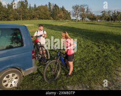 Ein junger Mann und eine Frau bereiten sich auf das Geländeradfahren vor und nehmen Elektro-Mountainbikes vom Fahrradträger im Wohnmobil ab. Stockfoto