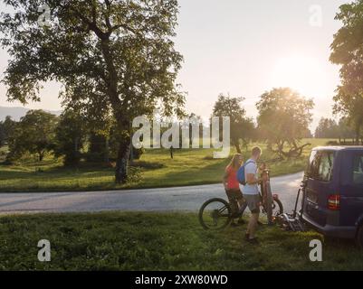 Ein junger Mann und eine Frau bereiten sich auf das Geländeradfahren vor und nehmen Elektro-Mountainbikes vom Fahrradträger im Wohnmobil ab. Stockfoto