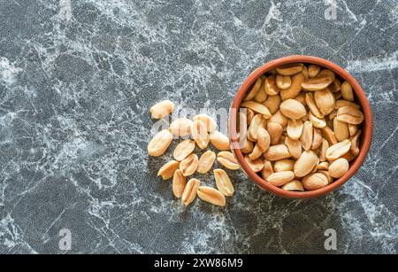 Erdnüsse in einer Schüssel, die daneben auf einer Marmoroberfläche verstreut ist Stockfoto