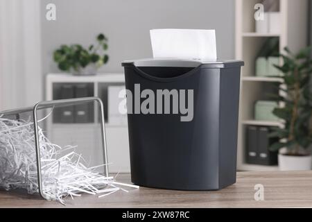 Zerstörung von Blättern mit Aktenvernichter und Papierstreifen in Metallbehälter auf Holztisch im Büro Stockfoto