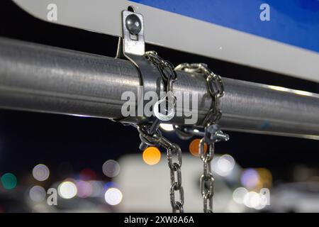 Nahaufnahme einer silbernen Kette und eines Vorhängeschlosses, die ein blaues Schild an einem Metallpfosten befestigen – mit verschwommenen Fahrzeugen. Aufgenommen in Toronto, Kanada. Stockfoto