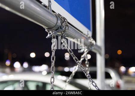 Nahaufnahme einer silbernen Kette und eines Vorhängeschlosses, die ein blaues Schild an einem Metallpfosten befestigen – mit verschwommenen Fahrzeugen. Aufgenommen in Toronto, Kanada. Stockfoto