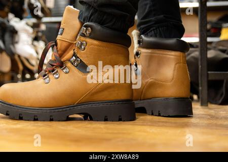 Braune Wanderschuhe aus Leder mit schwarzen Sohlen auf Holzboden - Person mit schwarzer Hose - Einzelhandelsgeschäft. Aufgenommen in Toronto, Kanada. Stockfoto
