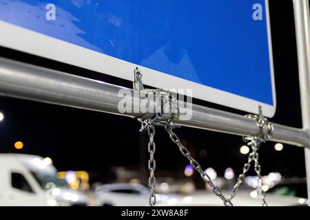 Nahaufnahme einer silbernen Kette und eines Vorhängeschlosses, die ein blaues Schild an einem Metallpfosten befestigen – mit verschwommenen Fahrzeugen. Aufgenommen in Toronto, Kanada. Stockfoto