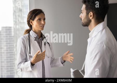 Doktor im weißen Mantel, der sich mit einem männlichen Kollegen unterhalten hat Stockfoto