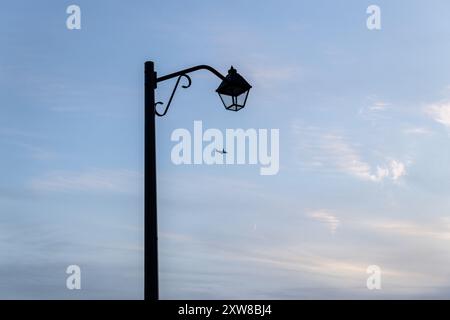 Vintage Straßenlaterne Silhouette gegen Dämmerungshimmel - Flugzeug in der Ferne - Mondsichel sichtbar. Aufgenommen in Toronto, Kanada. Stockfoto