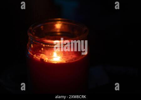 Leuchtende rote Kerze in einem Glasgefäß - warmes Licht beleuchtet die dunkle Umgebung - konzentrieren Sie sich auf die einzelne flackernde Flamme. Aufgenommen in Toronto, Kanada. Stockfoto