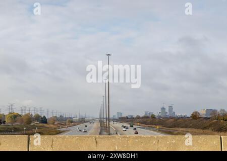 Bedeckter Himmel über einer belebten Autobahn, flankiert von Stromleitungen und Gebäuden - Fahrzeuge in Bewegung. Aufgenommen in Toronto, Kanada. Stockfoto
