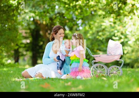 Familie mit Kindern genießt Picknick im Freien. Mutter mit neugeborenem Baby und Kleinkind entspannen in einem Park. Kleines Mädchen, das mit einem Kinderwagen spielt. Stockfoto