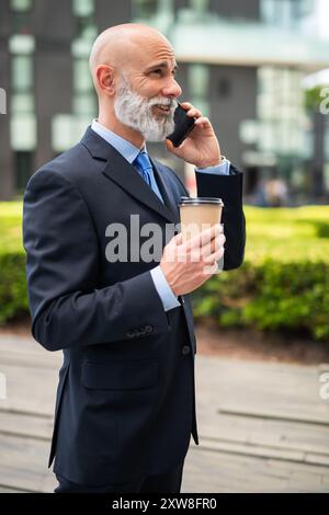 Kahler Geschäftsmann mit weißem Bart, der am Telefon spricht und Kaffee trinkt Stockfoto