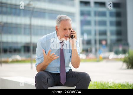 Ein wütender Geschäftsmann, der draußen das Telefon anschreit Stockfoto