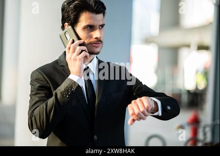 Geschäftsmann, der am Telefon die Zeit in einer modernen Stadt beobachtet Stockfoto