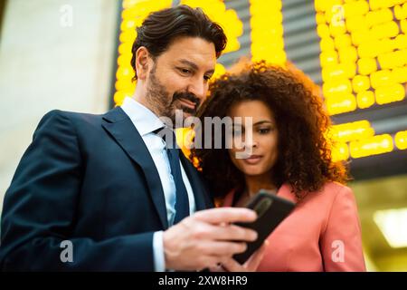 Ein Paar, das mit einem Smartphone den Fahrplan eines Bahnhofs überprüft Stockfoto