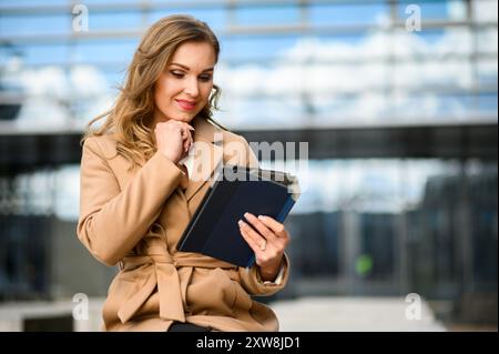 Eine Frau in braunem Mantel und weißem Hemd sieht sich eine Tablette an Stockfoto