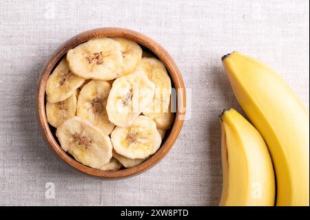 Bananenchips oder Bananenchips in einer Holzschale auf Leinenstoff. Gelbe knusprige, frittierte Bananenscheiben, bedeckt mit Zucker oder Honig. Stockfoto