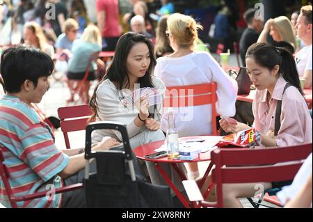 LONDON, GROSSBRITANNIEN. August 2024. Drei Chinesen, die eine traditionelle chinesische Karte spielen, um beim King's Cross Summer Sounds ein besseres Gedächtnis zu schaffen, veranstalten eine Feier der brasilianischen Kultur - Olayá im Coal Drops Yard, London, Großbritannien. (Quelle: Siehe Li/Picture Capital/Alamy Live News Stockfoto
