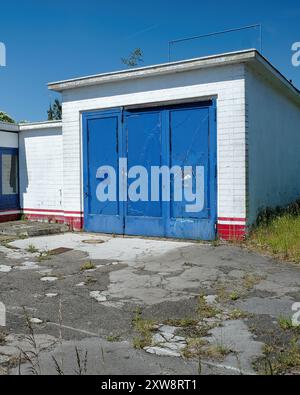 Alte Garage einer stillgelegten Tankstelle mit hellblauer Farbe. Verlorener Platz im Sommer und blauer Himmel. Stockfoto