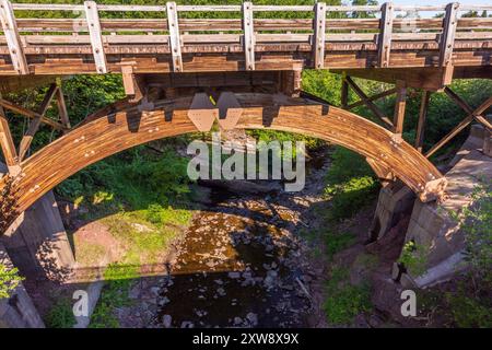 Eine Holzbrücke mit Bogenbalken über einem Bach. Stockfoto