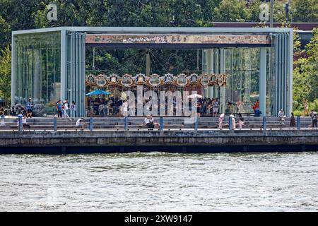 Jane’s Carousel steht im Schatten der Brooklyn Bridge. Das verglaste Vergnügungspark wurde aus Youngstown, Ohio, verlegt. Blick von der East River Fähre. Stockfoto