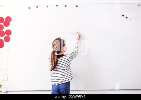 Eine Schülerin schreibt im Klassenzimmer auf der Tafel. Stockfoto