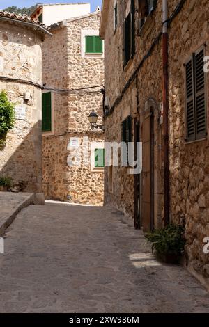 Charmante Gasse in Valldemossa, Mallorca, gesäumt von traditionellen Steinhäusern, bunten Holzläden und lebhaften Topfpflanzen an einem Sommertag. Stockfoto