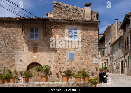 Charmante Gasse in Valldemossa, Mallorca, gesäumt von traditionellen Steinhäusern, bunten Holzläden und lebhaften Topfpflanzen an einem Sommertag. Stockfoto