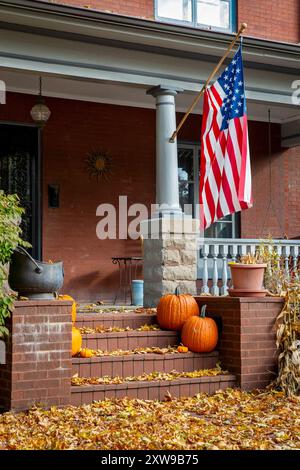 Die Veranda eines Hauses mit einer US-Flagge, herabfallenden Herbstblättern und einer Herbstkürbis-Präsentation für Halloween. Stockfoto