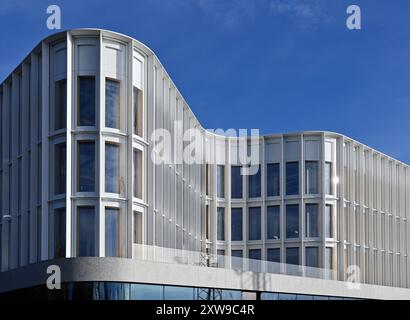 Das Bild zeigt ein modernes architektonisches Gebäude mit einer schlanken und wellenförmigen Fassade. Die Struktur verfügt über große, vertikal ausgerichtete Fenster, die von einem eingerahmt werden Stockfoto