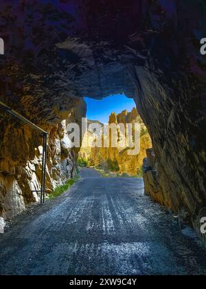 Wenn man durch einen alten Tunnel in der Nähe des Buffalo Bill Dam in Cody, Wyoming, blickt, sieht man Bergklippen in der Morgensonne. Eine alte Straße ist heute für den öffentlichen Verkehr gesperrt. Stockfoto