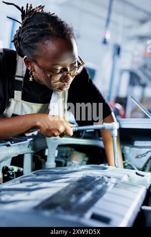 Die afroamerikanische Ingenieurin führt in der Autowerkstatt die Wartung des Kundenfahrzeugs durch, nachdem ihr Fahrzeug unerwartet abgeschaltet wurde. Zertifizierter Arbeiter in der Werkstatt, der den beschädigten Kraftstofftank des Fahrzeugs repariert Stockfoto