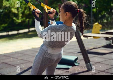 Eine Frau führt Krafttraining mit einem Suspensionstrainer in einem Freiluftpark durch. Sie konzentriert sich auf Fitness und Gesundheit und übt in lässigen, sportlichen Atts Stockfoto